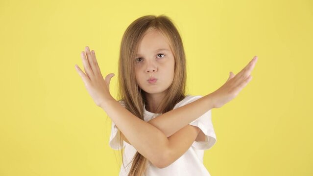 Dissatisfied angry little kid girl in white t-shirt isolated on yellow background studio. Childhood lifestyle concept. Swearing holding palm crossed hands, stop gesture