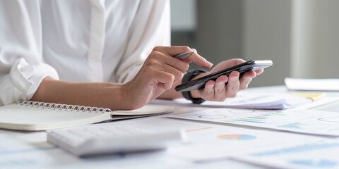 Accountant using mobile phone at office, analyzing business document with graph. Financial chart, marketing report. Accounting data analysis concept