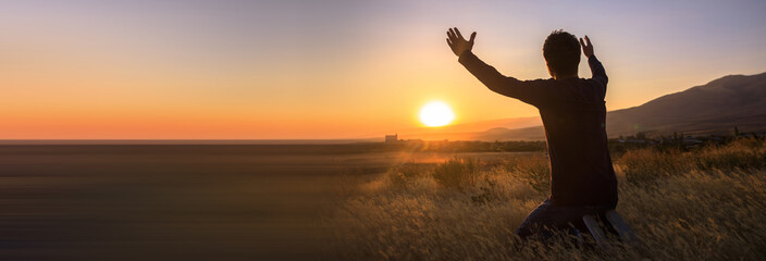 man with hands raised in the sunset