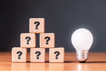 Many questions in stack of wood cubes with glowing light bulb, creativity comes from the questions,...