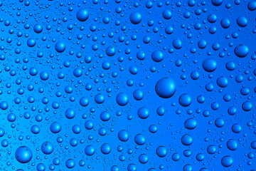 Bubbles and water drops in selective focus on glass, blue background.
