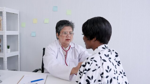 Senior female doctor nearing retirement age Using a stethoscope Listen to the lungs of an African single mother Who have symptoms of illness from the flu. In the hospital examination room