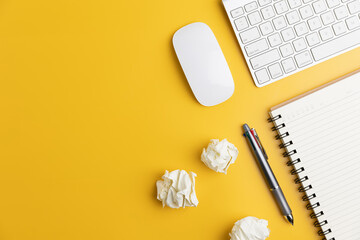 The home office with a pen, and notebook with a mouse on a yellow table with copy space. Top view, flat lay minimal yellow desk concept. Workspace desk with keyboard on yellow background.