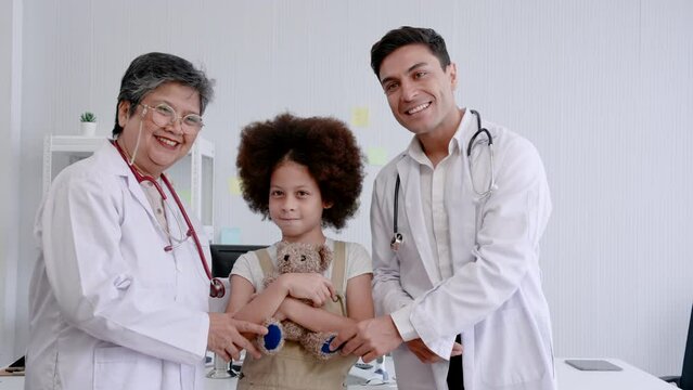 Asian pediatric doctor Elderly women and male medical assistant stands and talks with African child, holding a doll in hand. Familiarize yourself with the patient before performing a physical exam