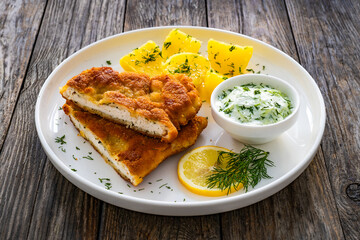 Crispy breaded seared chicken cutlet with boiled potatoes and cucumbers in cream on wooden table
