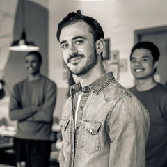 Portrait of young student looking at camera during leisure activity in recreation room at campus - Multi-ethnic classmates in background - Black and white editing with focus on the face