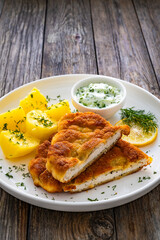 Crispy breaded seared chicken cutlet with boiled potatoes and cucumbers in cream on wooden table
