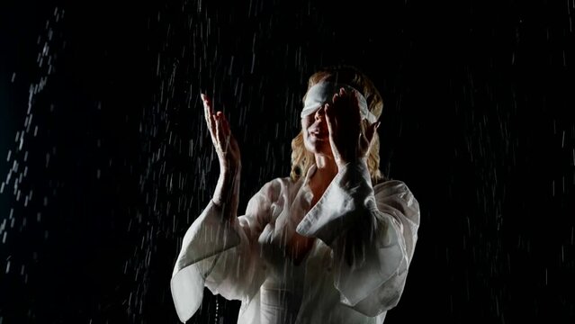 happy blindfolded woman enjoying rain in night, feeling water drops on her face