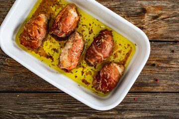 Stuffed pork loin with dried plums wrapped in cured ham in cooking pan on wooden table
