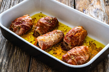 Stuffed pork loin with dried plums wrapped in cured ham in cooking pan on wooden table
