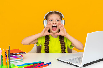 A child with headphones is studying on a laptop. A schoolgirl does her homework at the computer. The girl screams with her mouth wide open and holds her hands to her mouth like a megaphone.