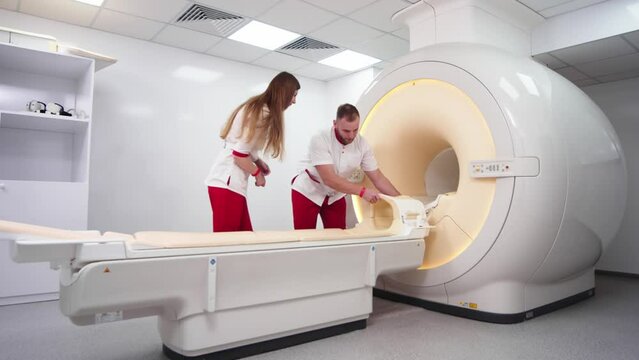 A rengolok doctor and an assistant are preparing equipment for a computed tomography scan in a modern medical center. Concept of treatment, healthy body and computer images.