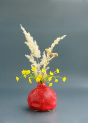 Natural  bouquet with dry decor. Still life with yellow buttercups and pampa. Сlay red vase in the form of a pomegranate on a gray background. Japanese art of flower arrangement. Ikebana arrangement.