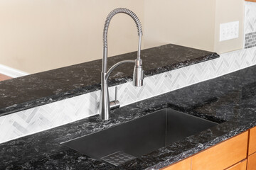 A kitchen faucet detail with wood cabinets, a black granite countertop, herringbone tile...