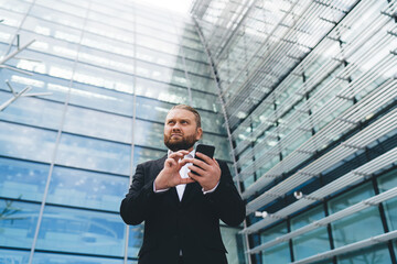 Confident businessman standing and browsing smartphone