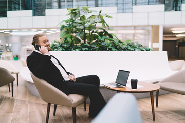 Cheerful corporate man talking on smartphone while sitting in executive lounge