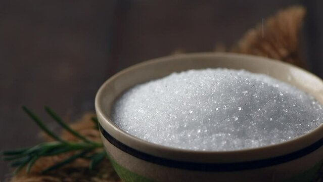 Pour white sugar into bowl on wood background, White sugar produced from sugar cane may be refined using bone char by a few sugar cane refiners