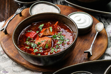 Ukrainian traditional beetroot soup - borscht in bowl with meat, rye bread and sour cream on bowl on rustic wooden background. Close up