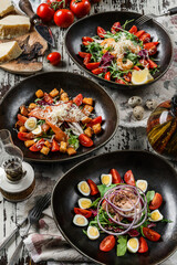 Assorted salads with tuna fish, shrimp, fillet salmon, vegetables and lettuce in plate on rustic wooden background. Healthy seafood, close up