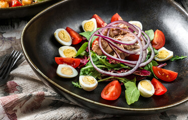 Healthy tuna salad with eggs, arugula, tomatoes, lettuce in plate on rustic wooden background. Healthy food, close up