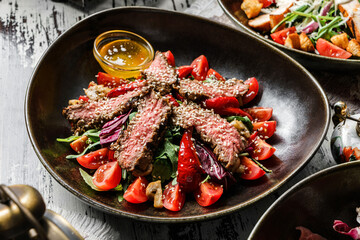 Healthy beef salad with sesame, arugula, tomatoes, lettuce in plate on rustic wooden background. Healthy food, close up