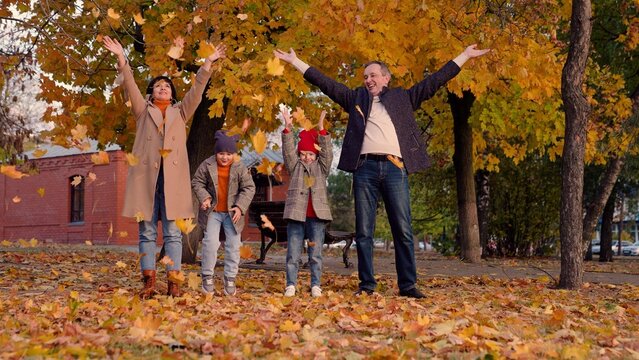 Happy family, child mom dad throwing yellow leaves up in autumn park, fun game. Baby, mom, dad play together, throw dry leaves in autumn outdoors. Family walk, mother, child, father, laughter, smiles