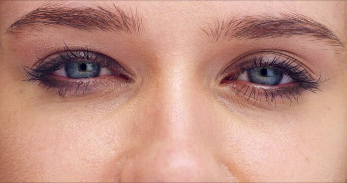 Closeup of woman with eyes blinking with her pupils dilating with beautiful long eyelashes and makeup. Macro zoom of a girl with optical eyesight and a human eyeball vision with iris and sclera.