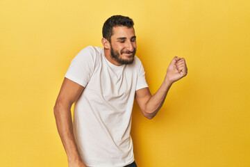Young Hispanic man on yellow background dancing and having fun.