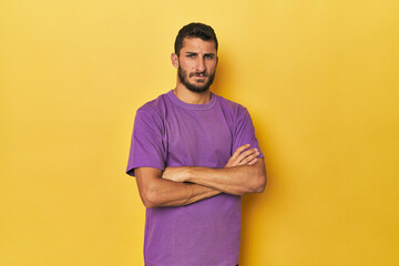 Young Hispanic man on yellow background suspicious, uncertain, examining you.