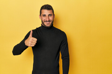 Young Hispanic man on yellow background smiling and raising thumb up