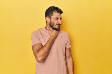 Young Hispanic man on yellow background suffers pain in throat due a virus or infection.