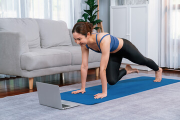 Asian woman in sportswear doing burpee on exercising mat as home workout training routine. Attractive girl engage in her pursuit of healthy lifestyle with online exercise training video. Vigorous