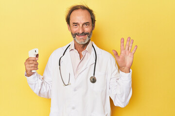 Doctor holding infrared thermometer in studio smiling cheerful showing number five with fingers.