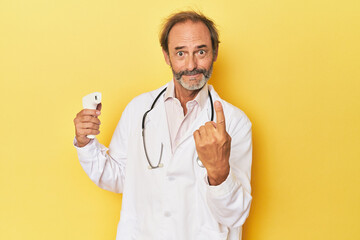 Doctor holding infrared thermometer in studio pointing with finger at you as if inviting come...