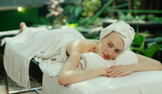 Beautiful young woman relaxes on a spa bed surrounded by nature. ready for a body massage. Attractive female in white towel lying peacefully during waiting for body massage. Close up. Tranquility