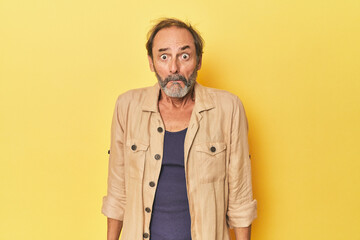 Caucasian middle-aged man in yellow studio shrugs shoulders and open eyes confused.