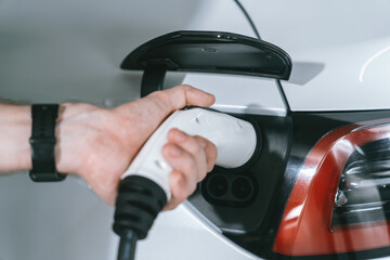 Young man travel with EV electric car to shopping center parking lot charging in downtown city...