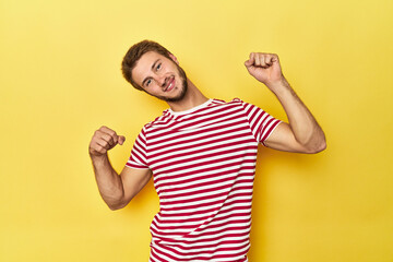 Young Caucasian man on a yellow studio background celebrating a special day, jumps and raise arms with energy.