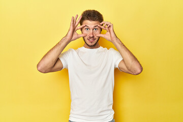 Fototapeta na wymiar Young Caucasian man on a yellow studio background keeping eyes opened to find a success opportunity.