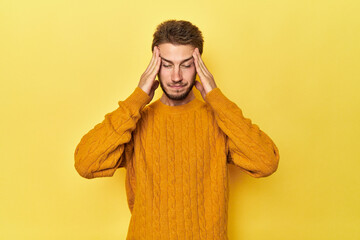 Young Caucasian man on a yellow studio background touching temples and having headache.