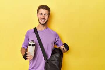 Athletic man with backpack, gloves, and water bottle on yellow studio backdrop