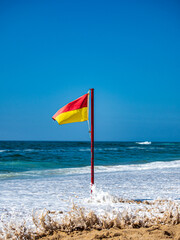 A restrictive flag is stuck in the sand on a beach on the ocean. - 664553582