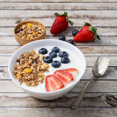 Yogurt with strawberry, blueberry and granola in a bowl over wooden table