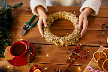 winter holidays, diy and hobby concept - close up of woman with decorations making christmas wreath...