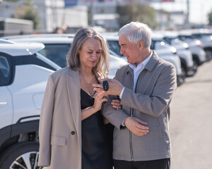Mature Caucasian couple standing by a car outdoors. Elderly man holding car keys. 