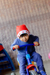Happy cute boy with a Christmas hat playing with a bicycle, in a moment of joy and festivity.