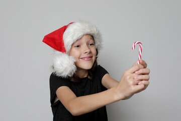 Portrait of a girl wearing a Santa Claus hat with a striped Christmas candy. Girl is delighted with Christmas