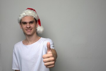 Teen boy young man wearing Santa Claus hat smiling and showing thumbs up