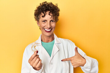 Doctor with invisible dental aligner on yellow person pointing by hand to a shirt copy space, proud...