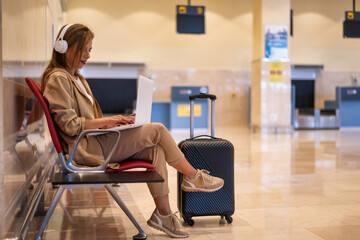 Business woman sitting in airport before trip using laptop. Business trip concept - obrazy, fototapety, plakaty